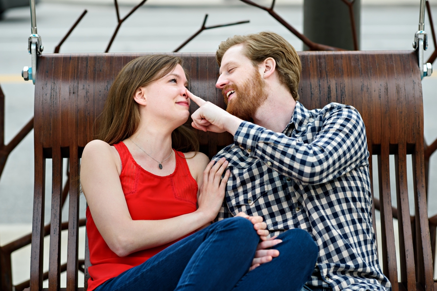 An engaged couple flirt on a swing outside of 30th street station in philadelphia during their engagement session.